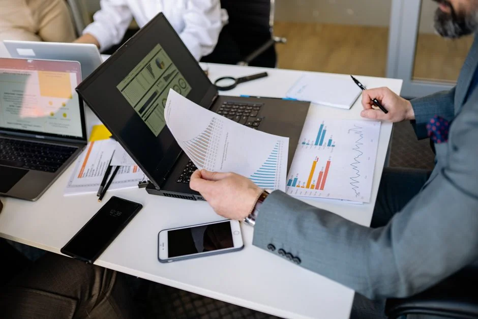 Person analyzes stock data with a smartphone and laptop, indoors.